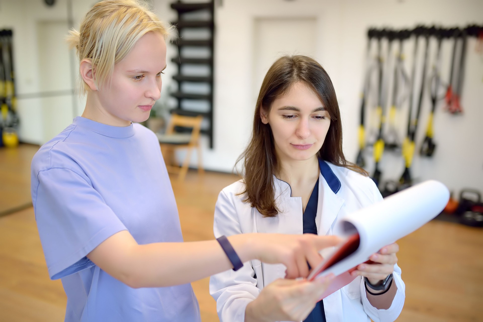 The rehab doctor conducts the patient's appointment in the gym. Before starting an individual session, the rehabilitologist make a patient survey and fills out a questionnaire.
